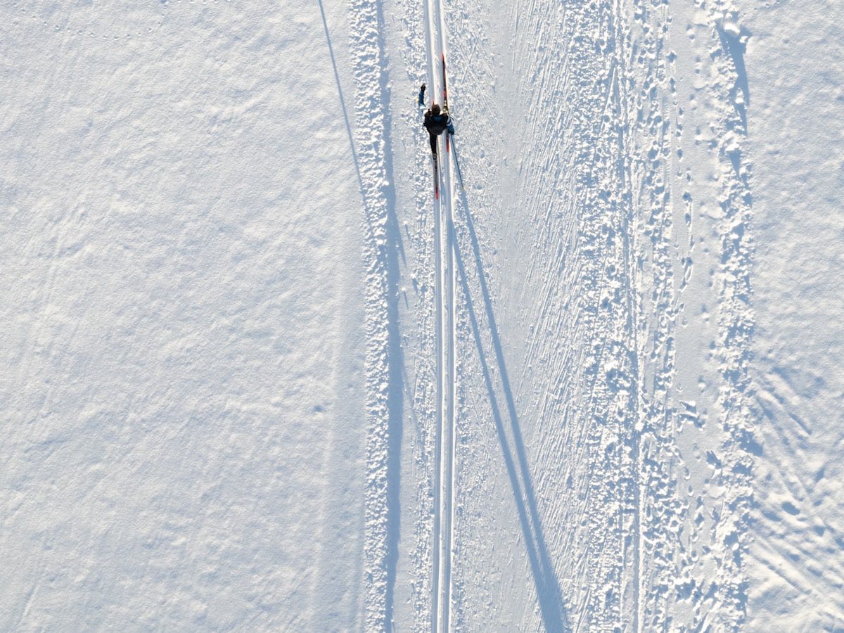 A cross-country skier in classic tracks casting a long shadow across open snow