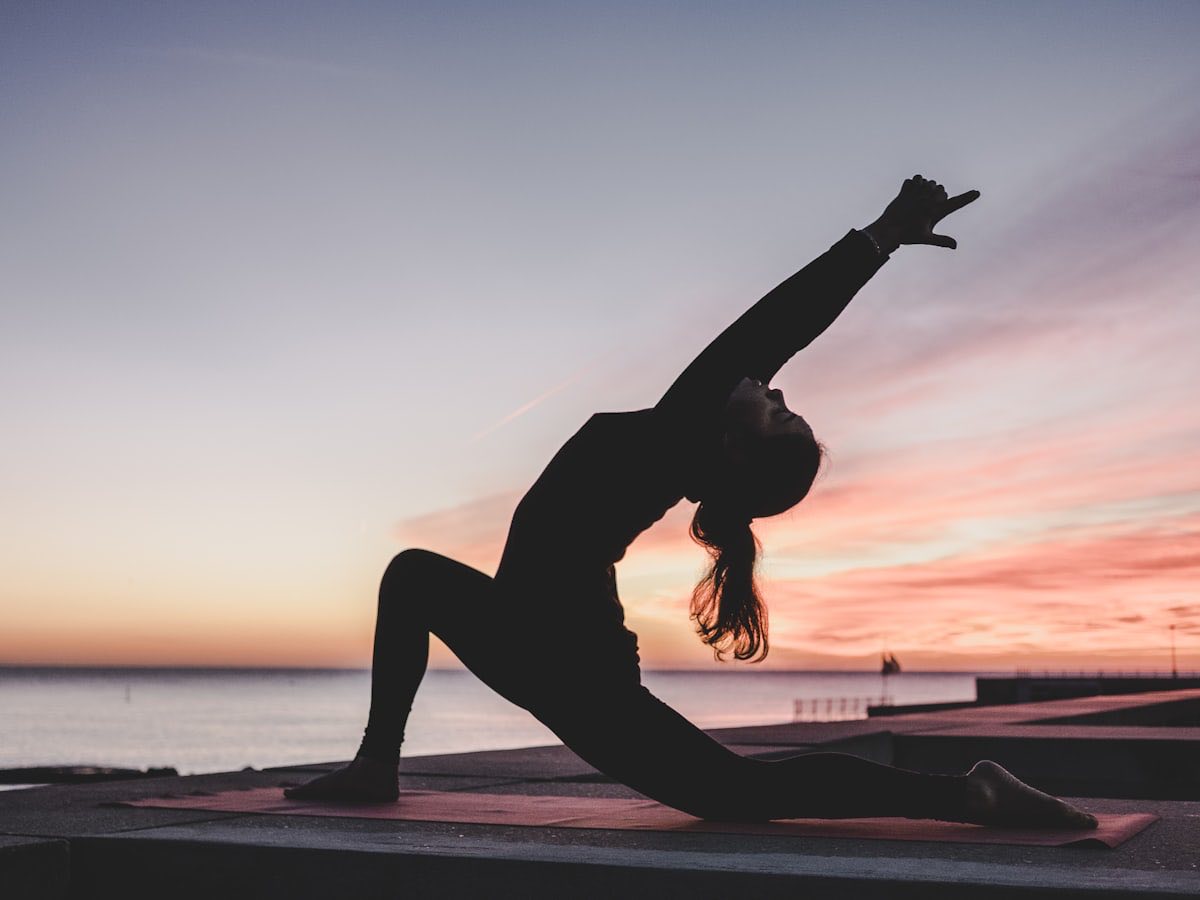 A woman in a yoga pose, silhouetted against a bright sky